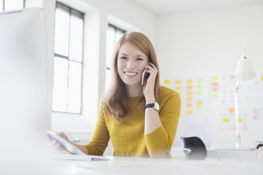 Junge Frau im Büro, die am Schreibtisch arbeitet und ein Smartphone benutzt - RBF003941