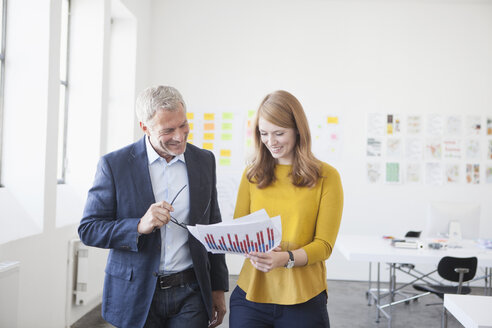 Geschäftsmann und Mitarbeiterin im Büro beim Studium von Infografiken - RBF003952