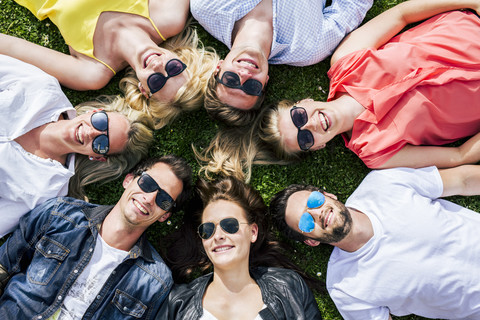 Glückliche Freunde mit Sonnenbrillen, die zusammen auf einer Wiese liegen, lizenzfreies Stockfoto