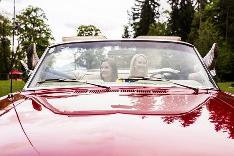 Zwei glückliche junge Frauen in einem Cabrio, die ihre Füße hochlegen, lizenzfreies Stockfoto