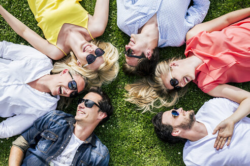 Glückliche Freunde mit Sonnenbrillen, die zusammen auf einer Wiese liegen - DAWF000463