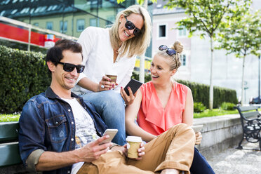 Glückliche Freunde auf einer Bank mit Blick auf Smartphones - DAWF000465