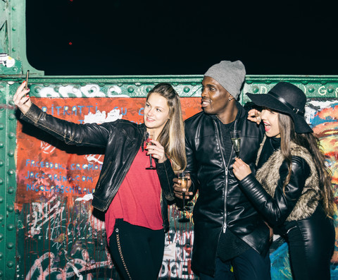 Friends with champagne glasses taking a selfie at graffiti wall at night stock photo