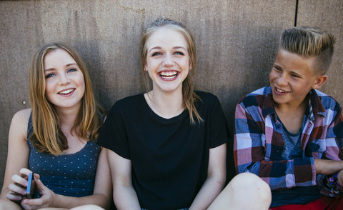 Three happy teenagers sitting outdoors stock photo