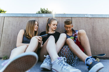 Three teenagers sitting outdoors with smartphones - AIF000181