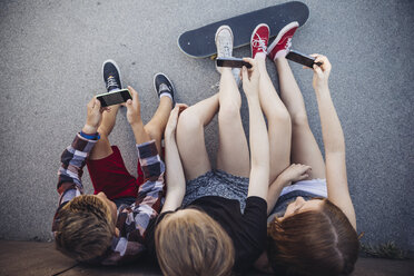 Three teenagers sitting outdoors with smartphones and skateboard - AIF000182