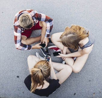 Three teenagers sitting outdoors with smartphones - AIF000183