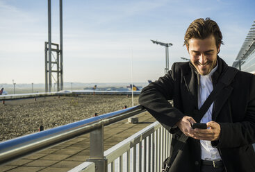 Deutschland, Frankfurt, Junger Geschäftsmann auf dem Flughafen mit Smartphone - UUF006324