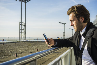 Deutschland, Frankfurt, Junger Geschäftsmann auf dem Flughafen mit Smartphone - UUF006325