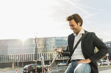Deutschland, Frankfurt, Junger Geschäftsmann in der Stadt mit Fahrrad, mit Mobiltelefon - UUF006351