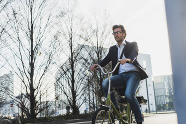 Germany, Frankfurt, Young businessman in the city riding bicycle - UUF006355