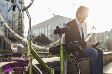Germany, Frankfurt, Young businessman with bike, sitting on wall, taking a break - UUF006356