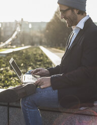 Deutschland, Frankfurt, Junger Geschäftsmann sitzt mit Laptop an der Wand - UUF006359