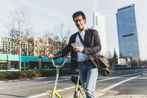 Deutschland, Frankfurt, Junger Geschäftsmann in der Stadt mit Fahrrad, mit Mobiltelefon, lizenzfreies Stockfoto