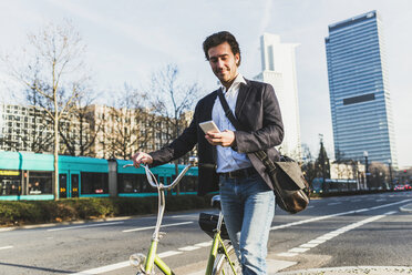 Germany, Frankfurt, Young businessman in the city with bicycle, using mobile phone - UUF006360