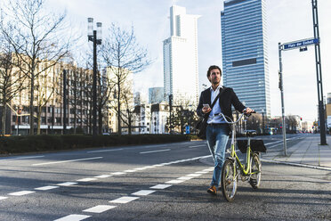 Deutschland, Frankfurt, Junger Geschäftsmann in der Stadt mit Fahrrad, mit Mobiltelefon - UUF006361