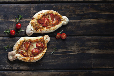 Zwei kleine Pizzen, Rosmarin und Kirschtomaten auf dunklem Holz - CSF026955