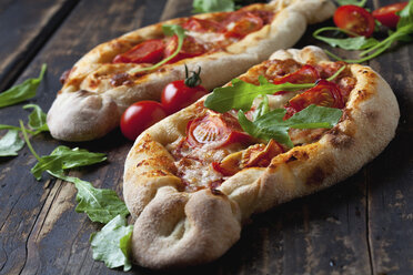 Small pizzas, rocket and cherry tomatoes on dark wood - CSF026956
