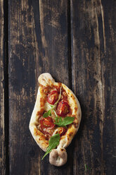 Kleine Pizza mit Rucola und Kirschtomaten auf dunklem Holz - CSF026957