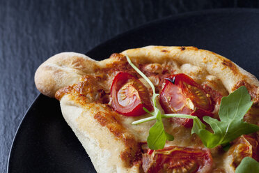 Kleine Pizza mit Rucola und Kirschtomaten auf schwarzem Teller und Schieferplatte - CSF026958