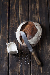 Knuspriges Brot, Brotmesser und Tütchen mit Salzkörnern auf dunklem Holz - CSF026968