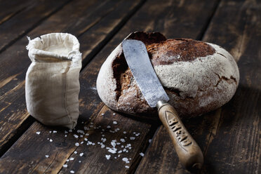 Knuspriges Brot, Brotmesser und Tütchen mit Salzkörnern auf dunklem Holz - CSF026969