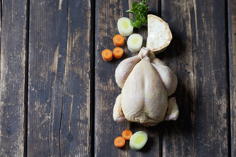 Rohes, mit Mais gefüttertes Hühnerfleisch und Grünzeug auf dunklem Holz, lizenzfreies Stockfoto