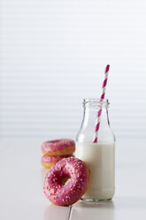 Glass bottle of milk and three doughnuts with pink icing on white ground - CSF026999