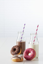 Zwei Glasflaschen mit Milch und Kakao und drei Krapfen mit verschiedenen Glasuren auf weißem Grund - CSF027000