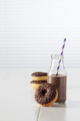 Glasflasche mit Kakao und drei Krapfen mit Schokoladenglasur auf weißem Grund - CSF027001