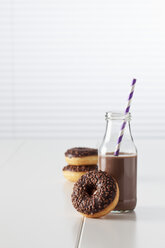 Glass bottle of cocoa and three doughnuts with chocolate icing on white ground - CSF027001