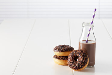 Glass bottle of cocoa and three doughnuts with chocolate icing on white ground - CSF027002