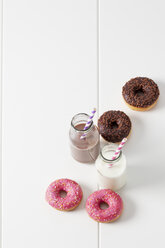 Two glass bottles of milk and cocoa and four doughnuts with different icings on white ground - CSF027005