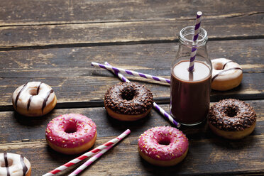 Glass bottle cocoa, drinking straws and doughnuts with different icings on dark wood - CSF027009
