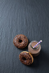 Glass bottle of cocoa and two doughnuts with chocolate icing on slate - CSF027012