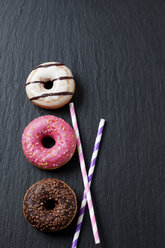 Three doughnuts with different icings and two drinking straws on slate - CSF027013