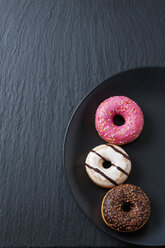 Three doughnuts with different icings on black plate and slate - CSF027014