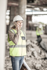 Frau in Arbeitsschutzkleidung telefoniert auf einer Baustelle - ZEF007836