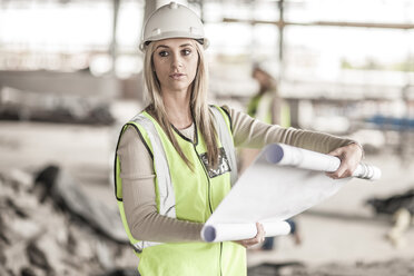 Woman in protective workwear holding building plan in construction site - ZEF007838