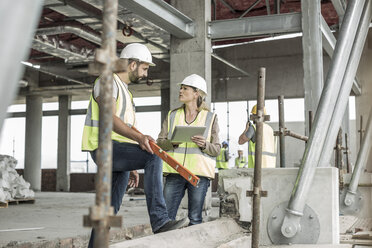 Woman in protective workwear and construction worker discussing in construction site - ZEF007851