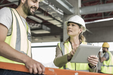 Frau in Arbeitsschutzkleidung und Bauarbeiter diskutieren auf einer Baustelle - ZEF007852