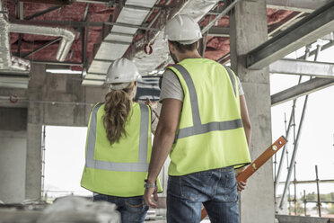 Frau in Arbeitsschutzkleidung und Bauarbeiter diskutieren auf einer Baustelle - ZEF007853