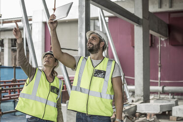 Frau in Arbeitsschutzkleidung und Bauarbeiter diskutieren auf einer Baustelle - ZEF007854