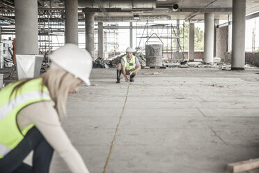 Bauarbeiter und Frau mit Maßband auf einer Baustelle - ZEF007867