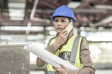 Woman in protective workwear on cell phone in construction site - ZEF007869