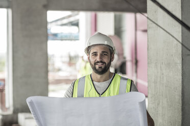 Porträt eines lächelnden Bauarbeiters mit Bauplan auf einer Baustelle - ZEF007876