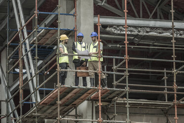 Construction workers and businessman discussing building plan on scaffolding - ZEF007886