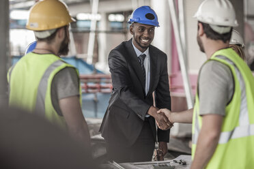 Two men wearing hard hats and hi vis vests, shaking hands