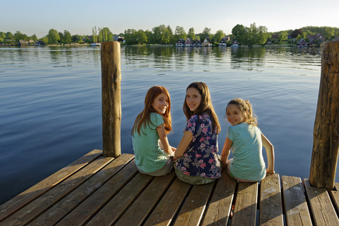 Deutschland, Mirow, drei Mädchen sitzen auf einem Steg am Mirower See, lizenzfreies Stockfoto