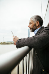 Österreich, Wien, Geschäftsmann steht auf der Reichsbrücke und schaut auf sein Smartphone - AIF000197